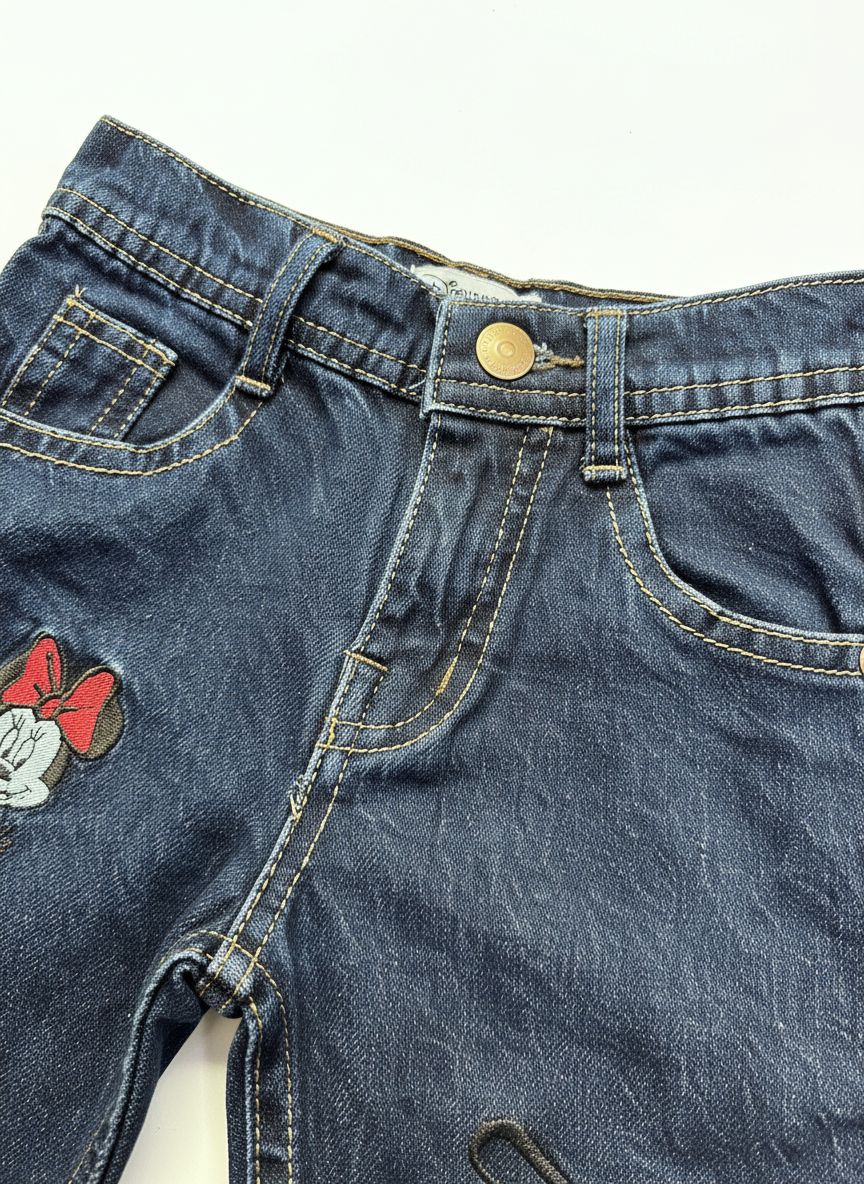 Close-up of girls' mid-blue denim Minnie embroidered jeans by Lil' Cubs, showing detailed Minnie Mouse embroidery on denim fabric.